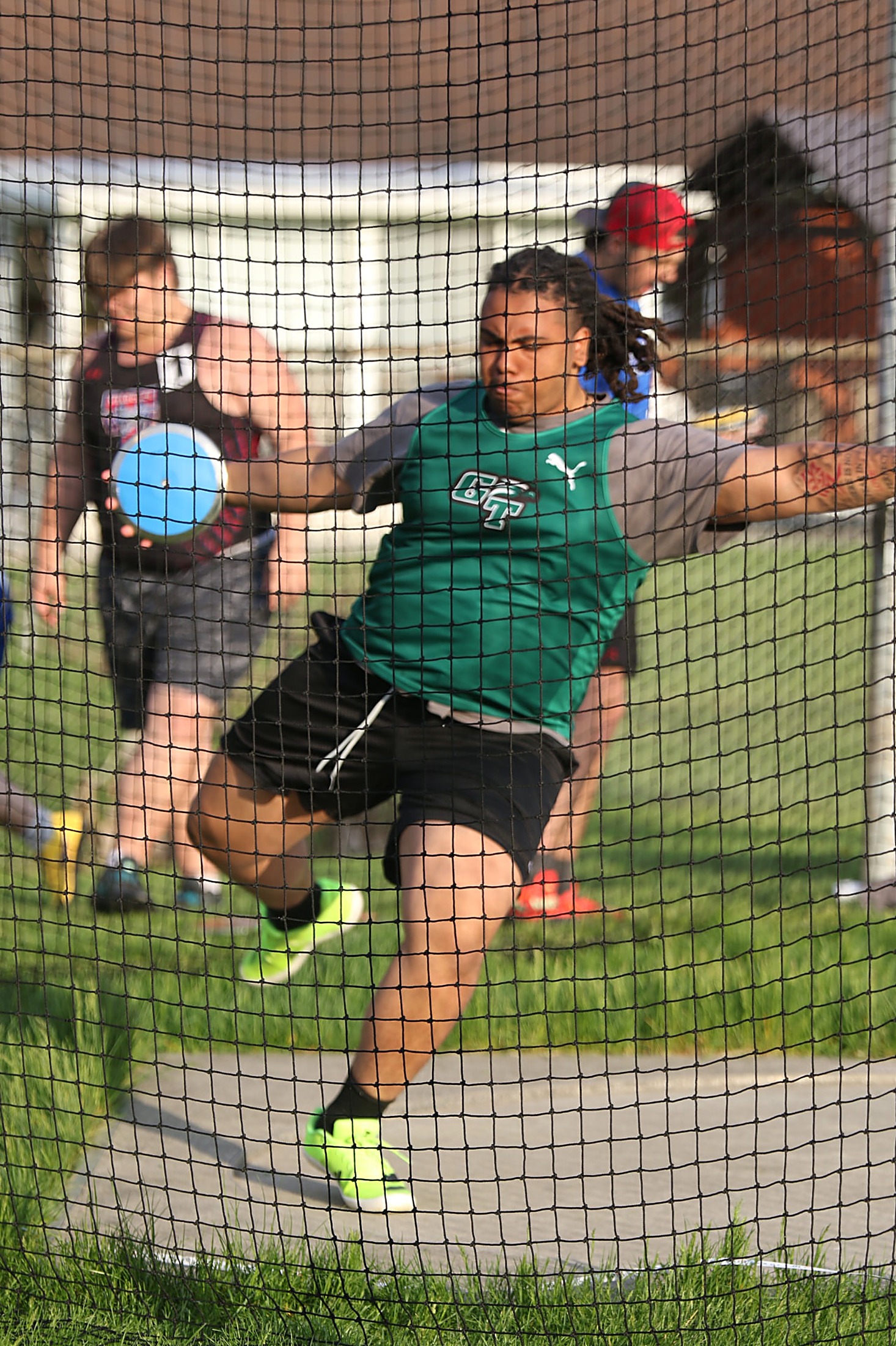 Green Tech field-event athlete winding up to release the discus inside the throwing cage